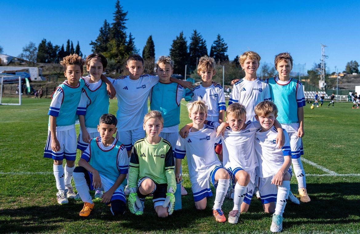 The squad in white kit and training bibs, lined up on the pitch under a clear sky