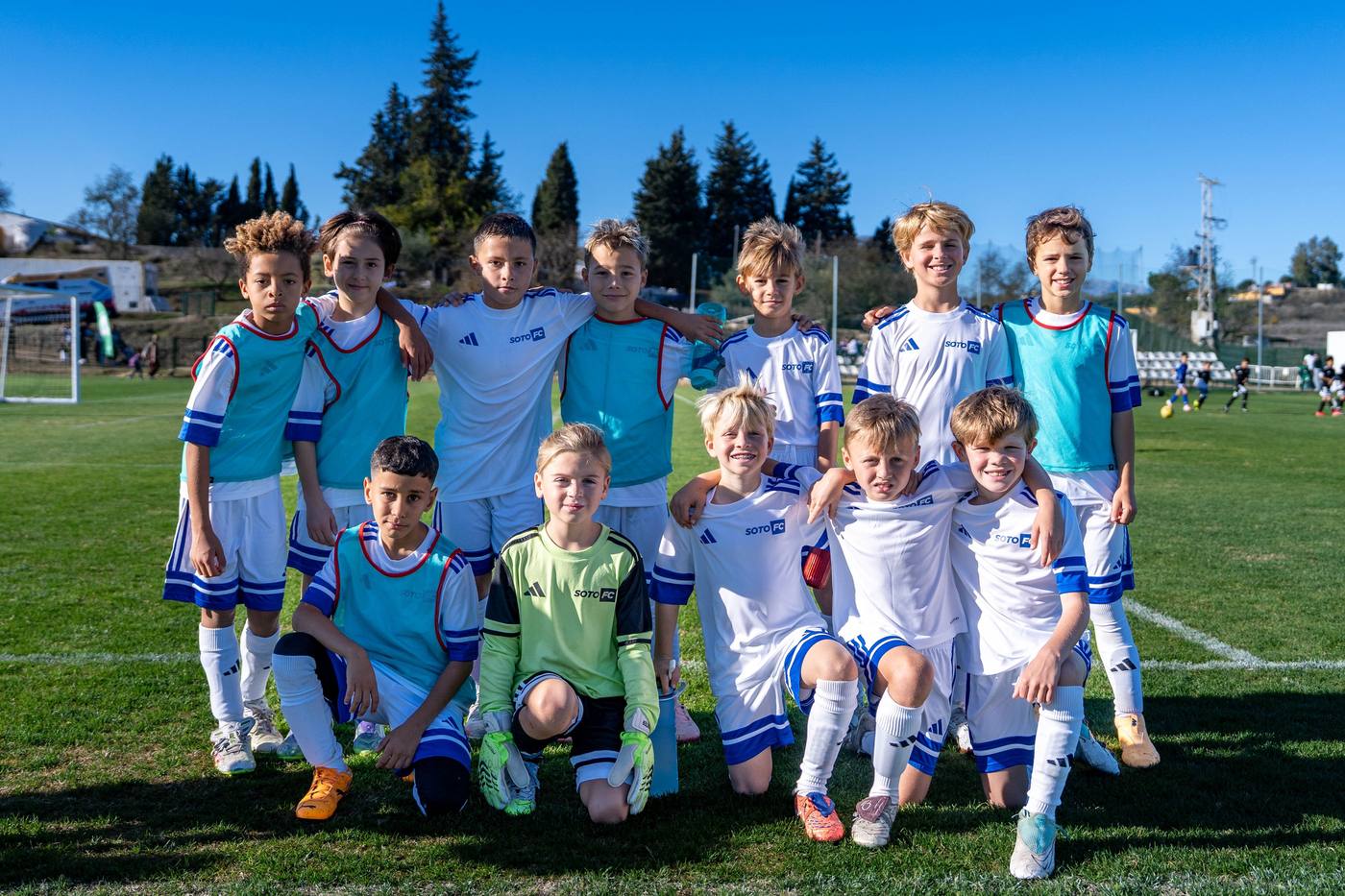 A Soto FC squad lined up on the pitch before a match, players in the white and blue kit with turquoise bibs