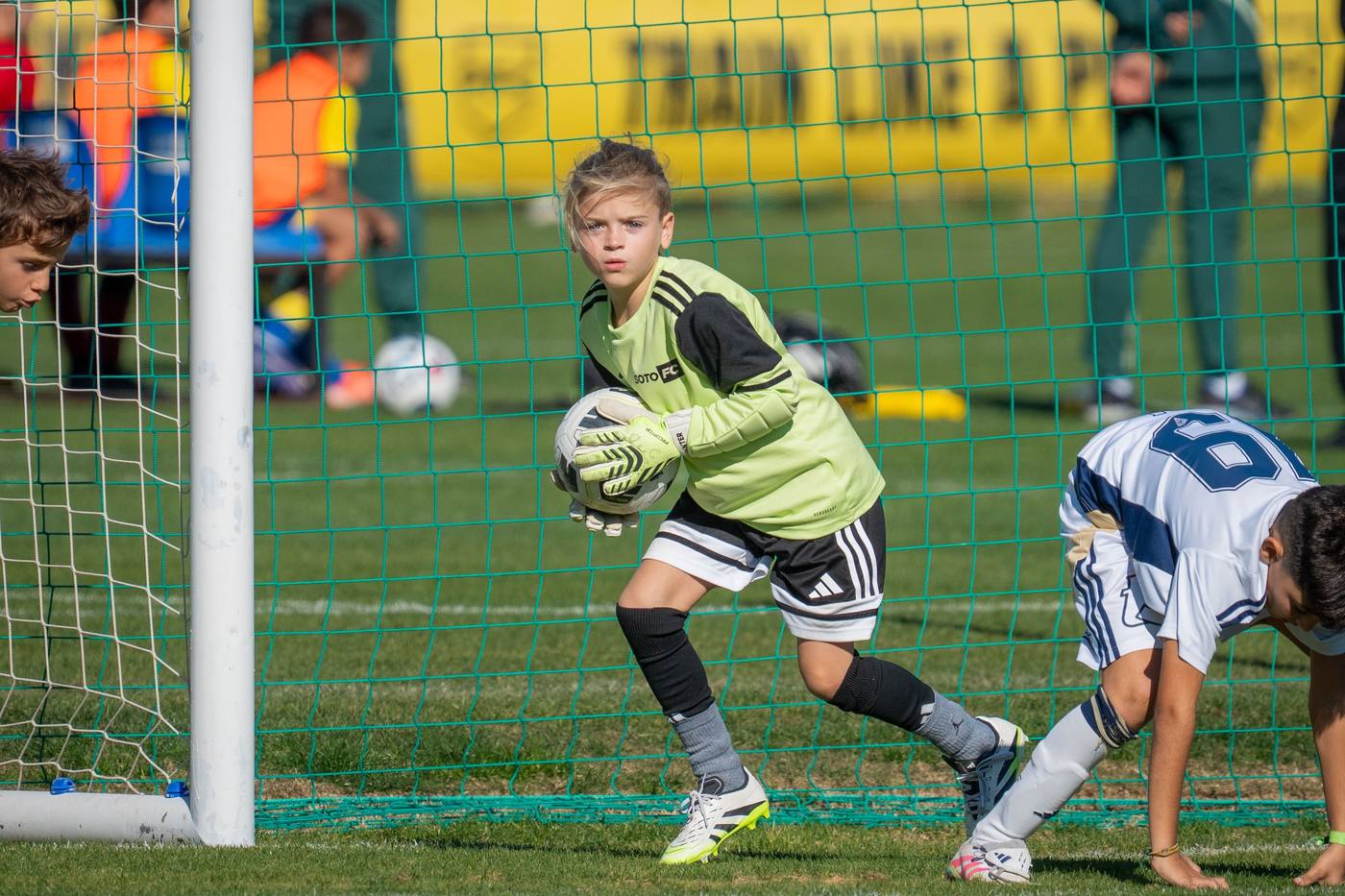 A Soto FC goalkeeper in a green shirt gathering the ball at the goal line during a match