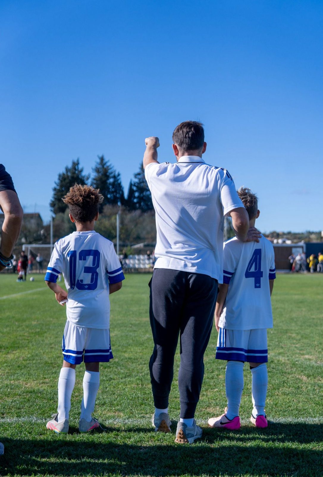 A coach with two players watching the game from the touchline
